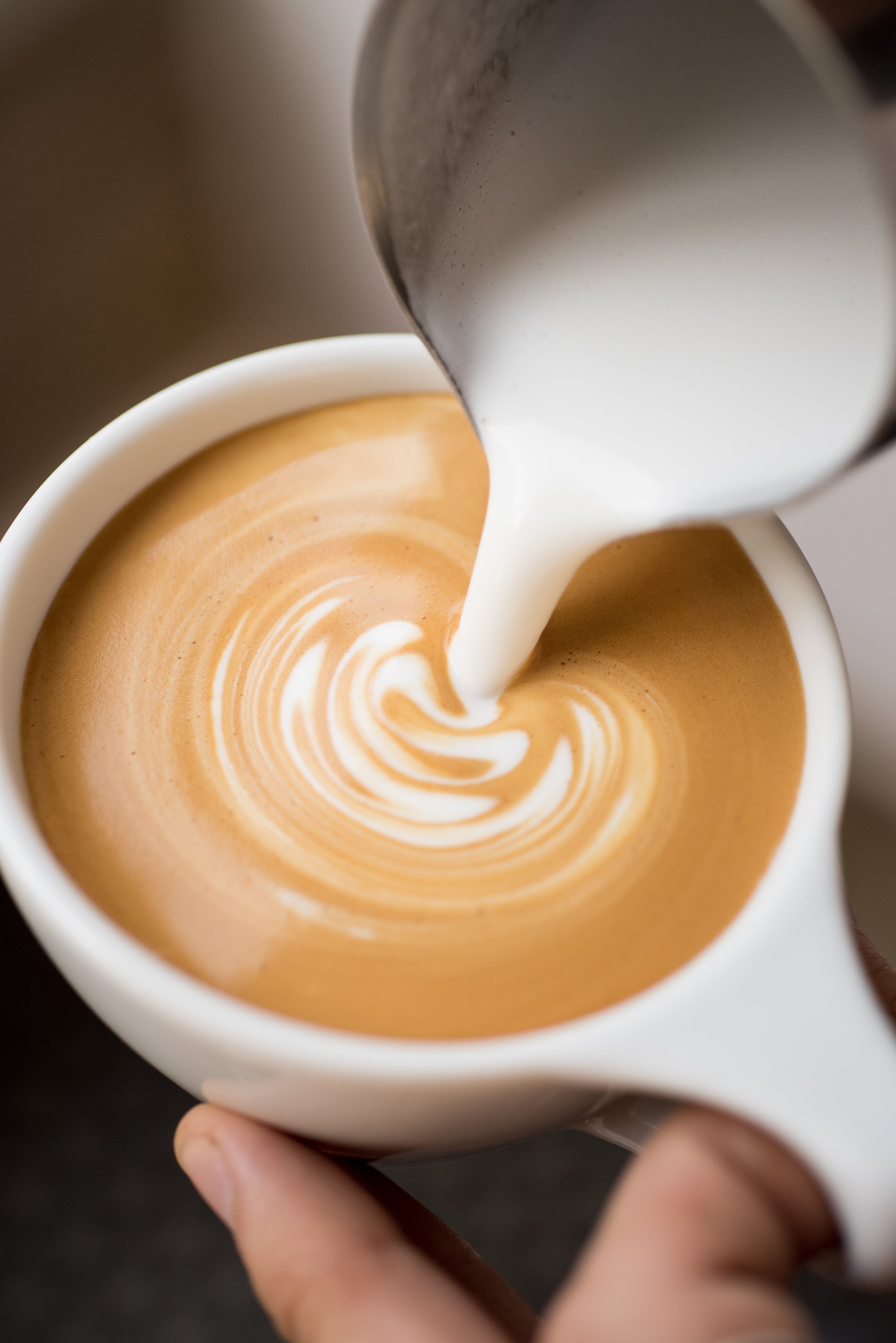 Pouring milk into a cup of coffee to create latte art.