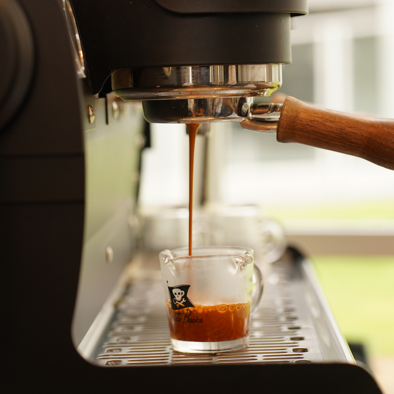 Espresso being poured from a machine into a small glass cup with a skull and crossbones design.